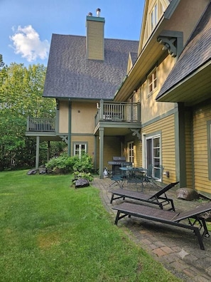 Ein zweistöckiges Haus mit überdachter Terrasse, Grill und Gartenmöbeln.