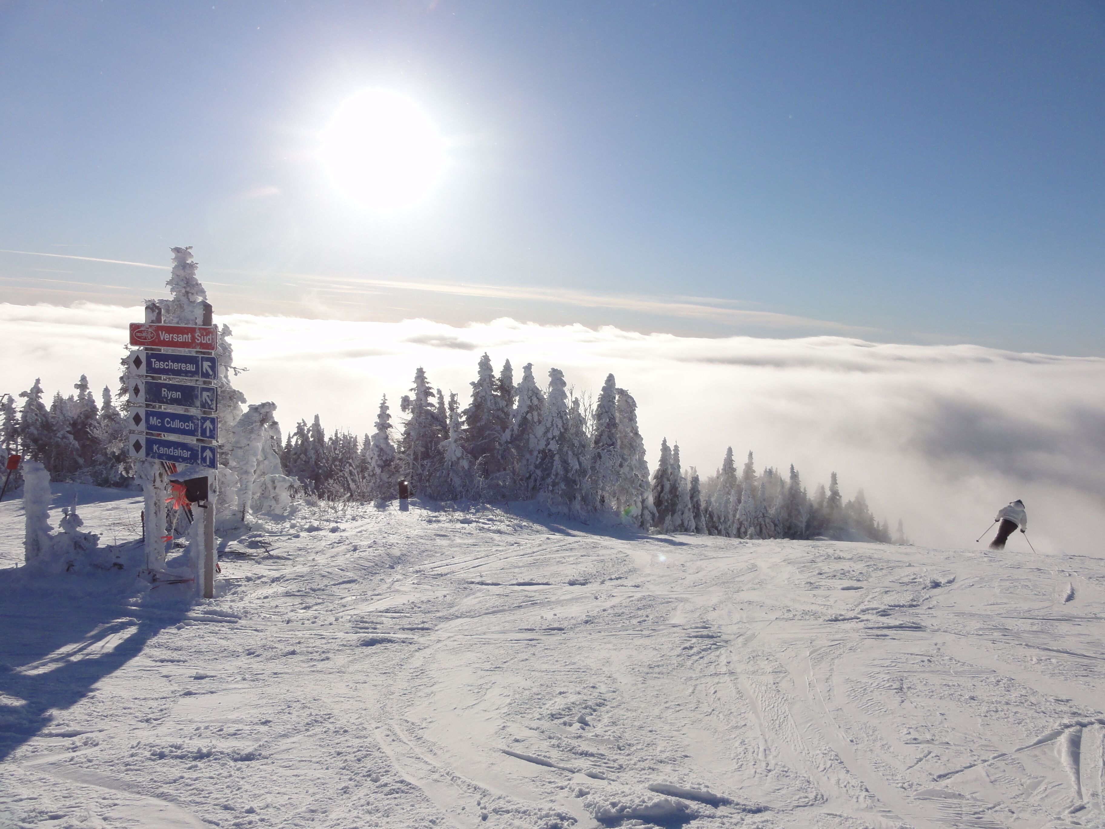 A snow-covered ski slope with a signpost indicating directions to various ski runs.