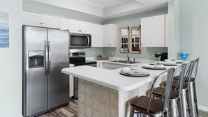 A modern kitchen with stainless steel appliances, white cabinetry, and a central island with bar stools. - Gulfside 215 ~ Ocean Views ~ Beach Service ~ Destin West! (Fort Walton Beach)