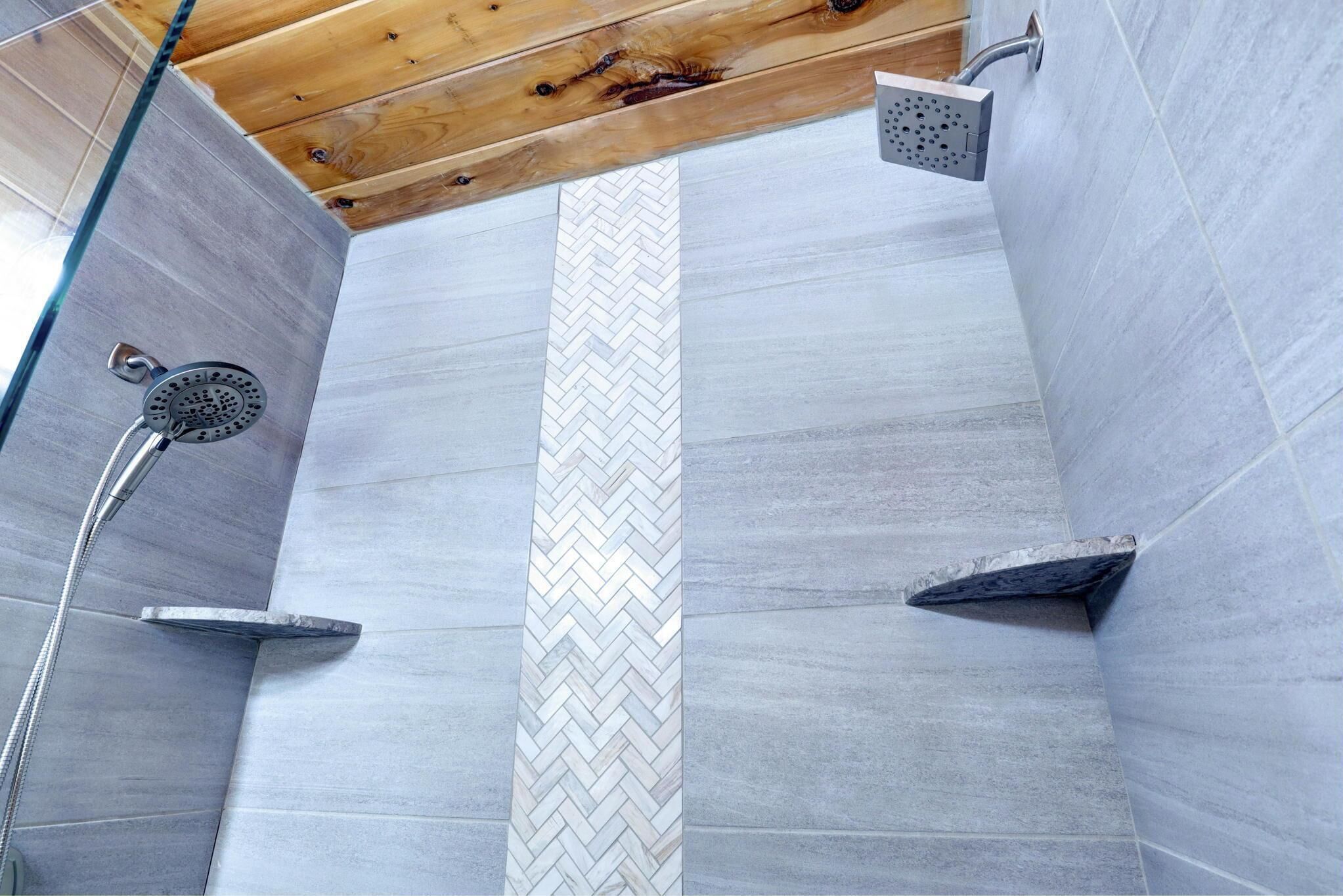 A shower area with a herringbone tile pattern, a wooden ceiling, and a showerhead.