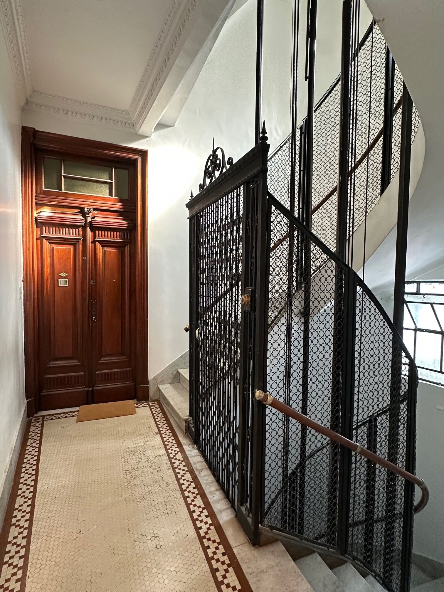 Eine Holztür mit Glasfenster, ein schwarzes Metallgitter und eine Wendeltreppe mit Metallgeländer.