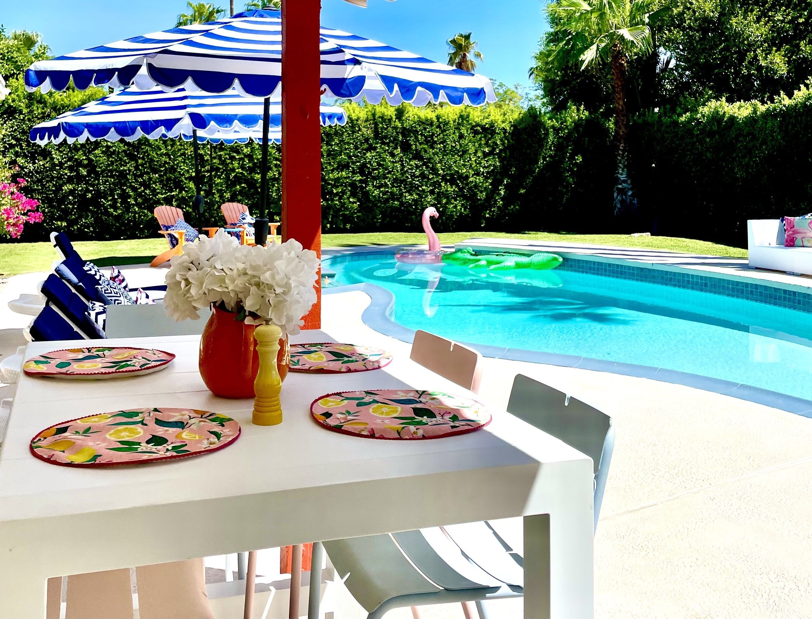 A poolside area with a table set for dining, surrounded by blue and white striped umbrellas.