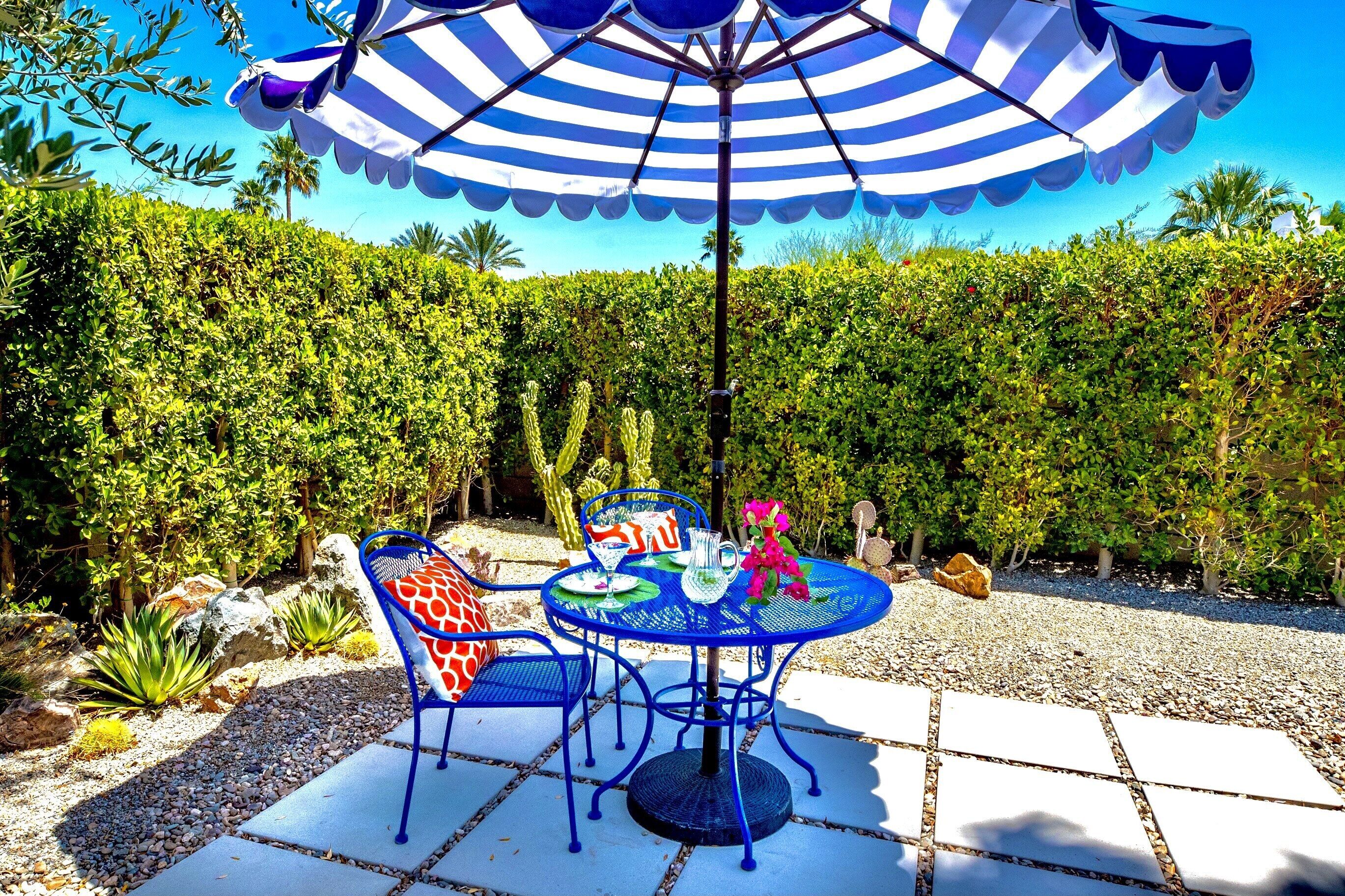 Une terrasse extérieure avec une table ronde, des chaises bleues et un parasol à rayures.