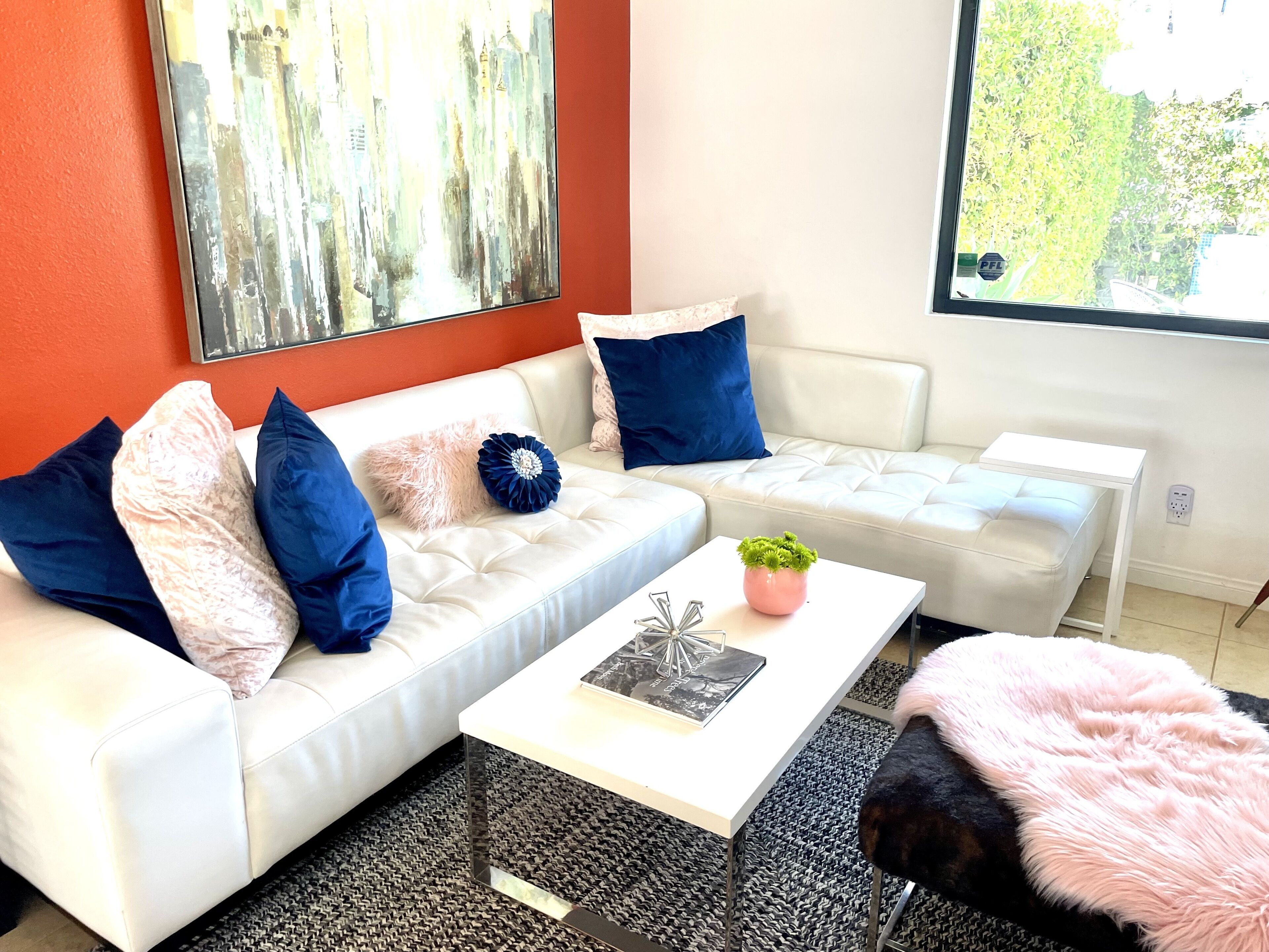 A modern living room with a white sofa, a coffee table, and a pink fluffy rug.