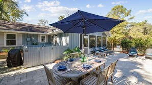 An outdoor patio with a wooden table and chairs, a large umbrella, and a screened porch area with lounge chairs. - Pet Friendly Home w/ Screened Porch & Pool (Hilton Head Island)