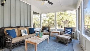 A covered outdoor seating area with a ceiling fan, wicker furniture, and a view of trees through large windows. - Pet Friendly Home w/ Screened Porch & Pool (Hilton Head Island)