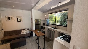 A compact kitchen with a built-in stove, a refrigerator, and a window with a view of greenery. - Paradise! Beach Rental with Private Pool! (Esterillos Oeste)