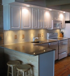 A kitchen with white cabinets, a stainless steel stove, and a microwave. There are two stools and a sink. - 4 Bedroom 2 1/2 Bath Ocean Front Townhouse with Outdoor Pool (Ocean City)