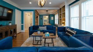 Un amplio salón con un sofá azul grande, una mesa de centro de madera y un televisor montado en la pared.