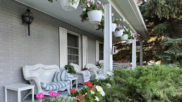 A porch with wicker furniture, hanging flower pots, and a brick wall. - Charming Victorian-Style Guest House (Cody)