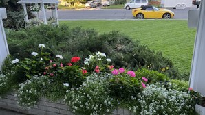 A residential street with a garden in the foreground, a gazebo, and parked cars including a yellow convertible. - Charming Victorian-Style Guest House (Cody)
