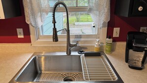 A stainless steel kitchen sink with a modern faucet, a soap dispenser, and a coffee maker on the counter. - Charming Victorian-Style Guest House (Cody)