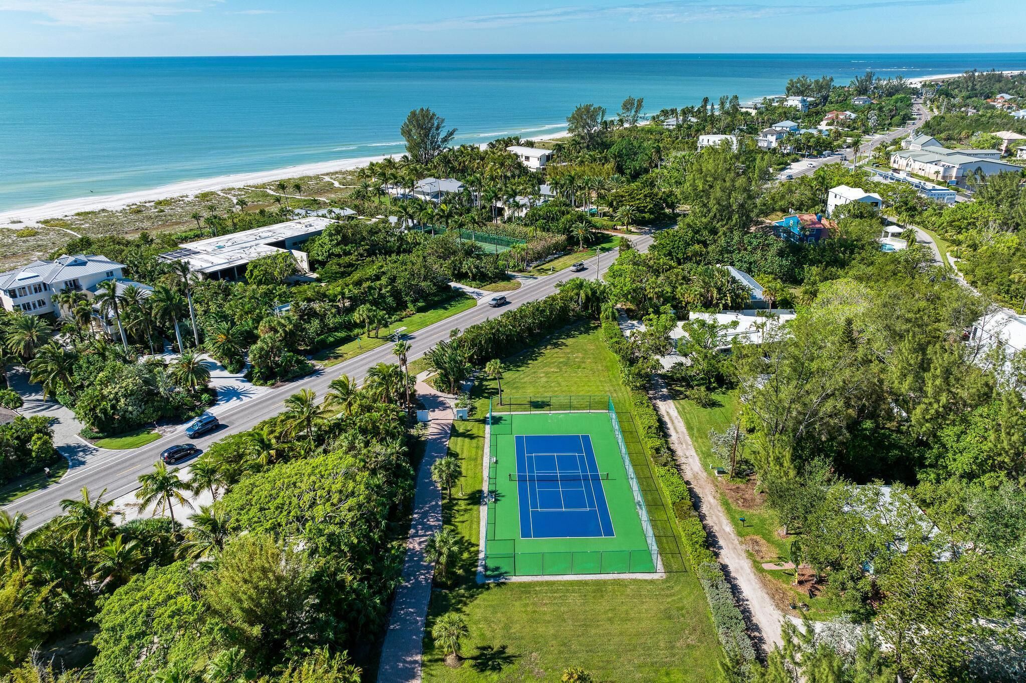 Vista aérea de una zona residencial con una cancha de tenis, una playa y una carretera.