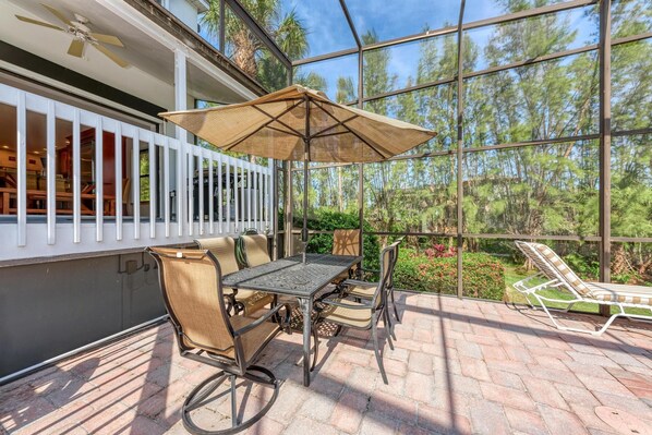 Un patio al aire libre con una mesa, sillas, un parasol y vistas a los árboles circundantes.