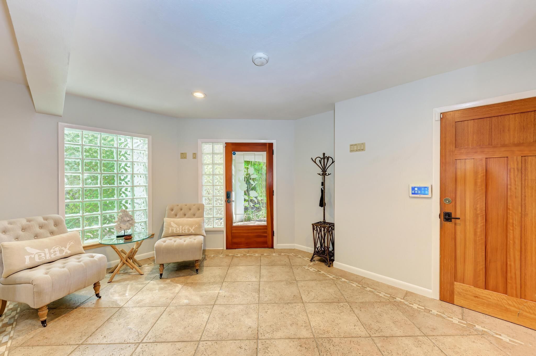 A spacious room with a large wooden door, a glass door leading outside, and a seating area with a cushioned chair and a small table.