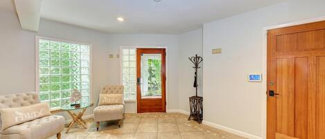 A spacious room with a large wooden door, a glass door leading outside, and a seating area with a cushioned chair and a small table.
