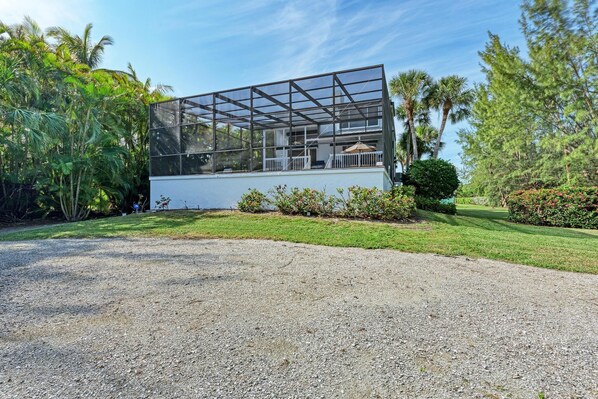 A modern glass house with a white exterior, surrounded by lush greenery and a gravel driveway. - Hidden Bay/Beach Paradise (Longboat Key)