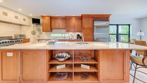 Een moderne keuken met houten kastjes, een groot eiland, roestvrijstalen apparatuur en uitzicht op de omgeving.