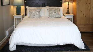 A neatly made bed with white bedding and patterned pillows, flanked by two bedside tables with lamps, a framed picture above the bed, and a wooden wardrobe to the right. - The Perfect Cottage For A Family Vacation At The Lake (Cultus Lake)