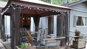 A covered outdoor seating area with a table and chairs, a wooden deck, and a small garden planter. - The Perfect Cottage For A Family Vacation At The Lake (Cultus Lake)