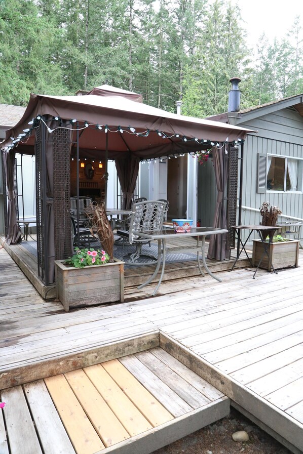 A covered outdoor seating area with a table and chairs, a wooden deck, and a small garden planter.