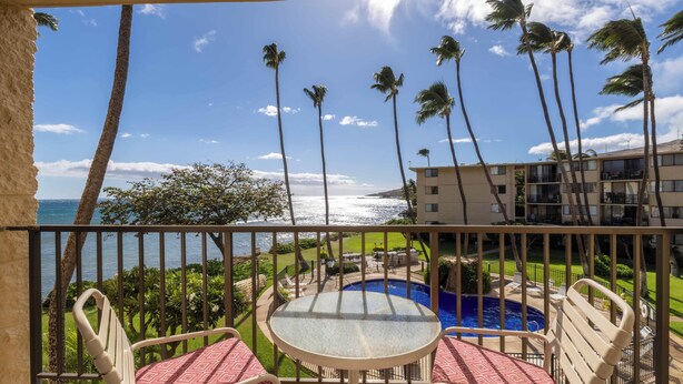 A balcony with a glass table and chairs, overlooking a swimming pool and a view of the ocean with palm trees. - Oceanview Kanai A Nalu 316 Great Views Split AC Pool Great Value (Wailuku)
