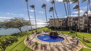 A circular pool with a surrounding deck, palm trees, and a view of the ocean. - Oceanview Kanai A Nalu 316 Great Views Split AC Pool Great Value (Wailuku)