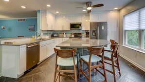 A modern kitchen with white cabinets, a central island with bar stools, a built-in oven, and a ceiling fan.