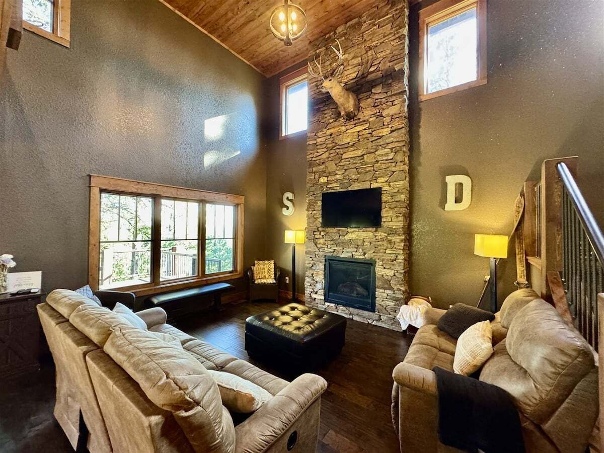 Una sala de estar acogedora con sofás de cuero, una chimenea de piedra y un ventanal grande.