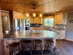 A kitchen with wooden cabinets, a central island with stools, and a stone backsplash. - Eagle View Lodge at Terry Peak (Lead)