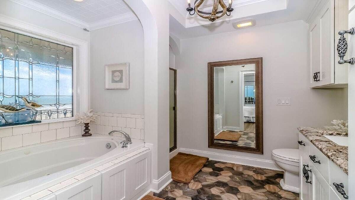 A bathroom with a bathtub, a toilet, and a large mirror.