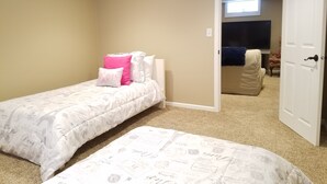 Een slaapkamer met twee bedden, beige wanden en een deur naar een andere kamer.