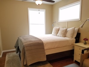 A bedroom with a bed, bedside table, lamp, window, and ceiling fan.