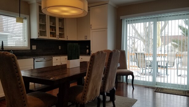 Een eetruimte met een houten tafel en stoelen, een hanglamp en uitzicht op de omgeving via een schuifdeur.