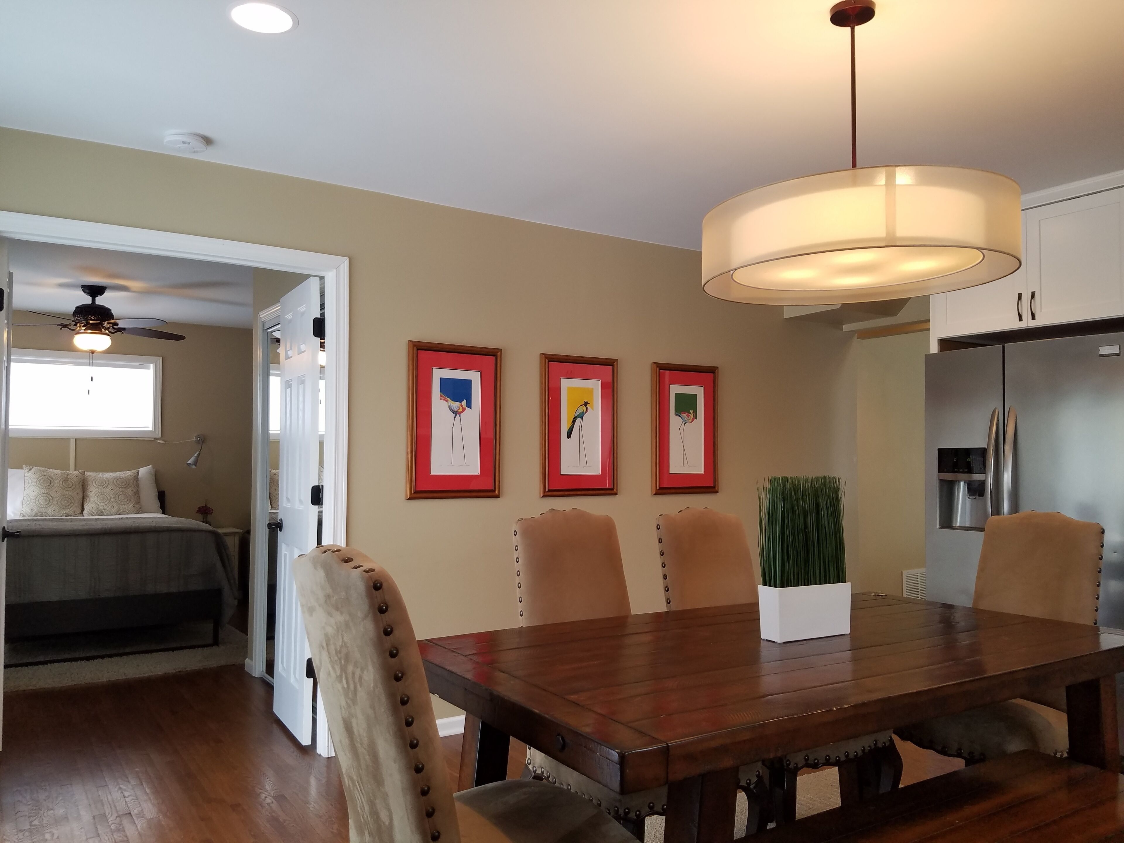 A dining area with a wooden table and chairs, a ceiling fan, and framed artwork on the wall.