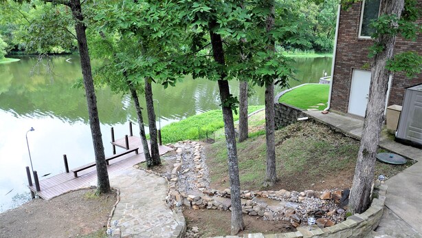 Um pátio à beira do lago com degraus de pedra, um deck de madeira e um muro de contenção de pedra.