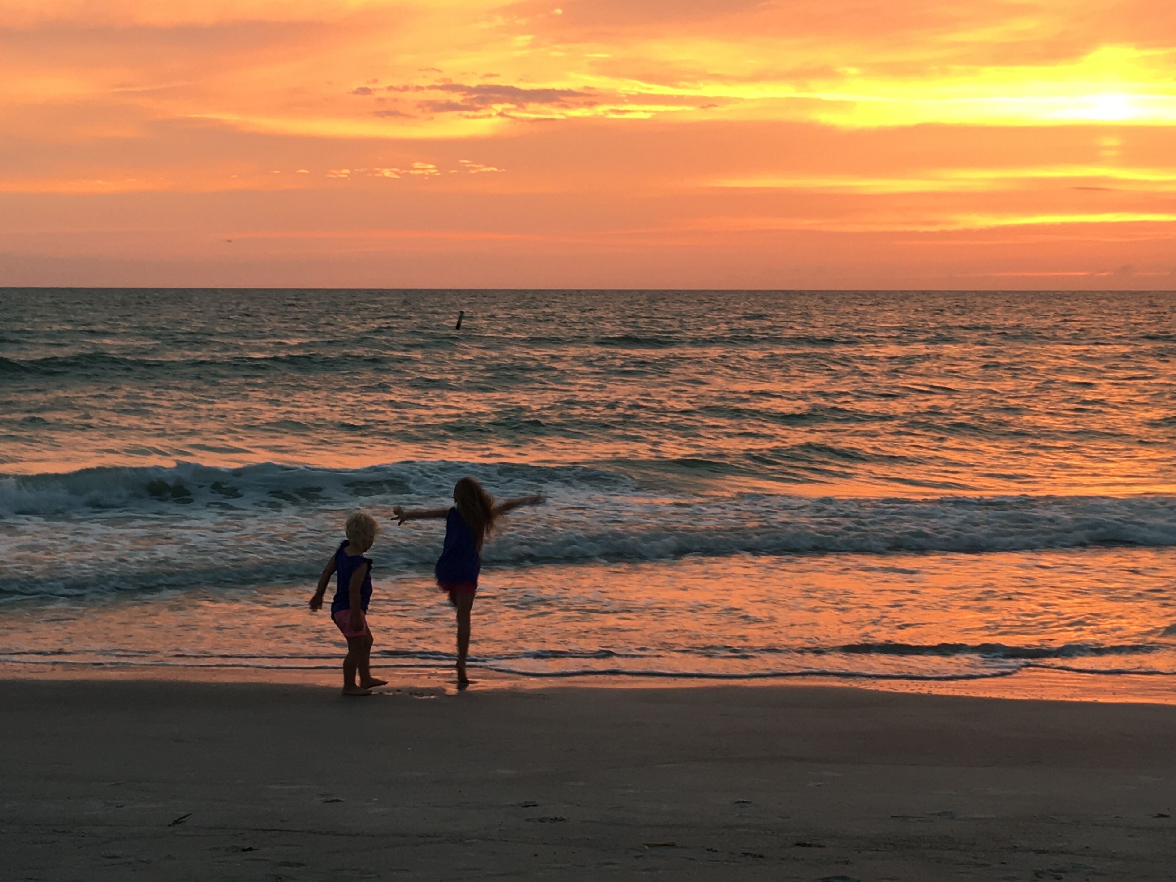 A beach scene with two people standing near the water's edge during sunset.