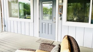 A porch with a grey door, two windows with blinds, a wicker chair, and a cushion. - Live like a local. Heated Pool, steps to the Beach. 2nd floor unit. Unit B (Indian Rocks Beach)