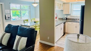 A modern kitchen with white cabinets, a built-in microwave, and a sink. There is a dining area with a table and chairs, and a black leather sofa with decorative pillows. - Live like a local. Heated Pool, steps to the Beach. 2nd floor unit. Unit B (Indian Rocks Beach)