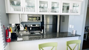 A modern kitchen with white cabinets, stainless steel appliances, and a granite countertop. - Live like a local. Heated Pool, steps to the Beach. 2nd floor unit. Unit B (Indian Rocks Beach)