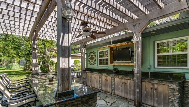 Una cocina exterior con encimera de piedra, armarios de madera y una estructura de pérgola.