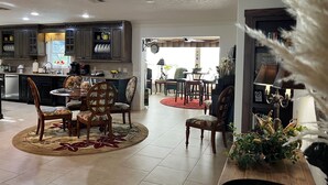 Una cocina amplia con armarios oscuros, un comedor con sillas estampadas y una sala de estar con alfombra roja.