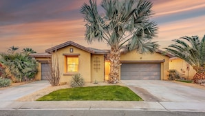 A residential house with a garage, a well-maintained lawn, and palm trees.