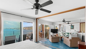 Et hotelværelse med balkon, seng, sofa, fjernsyn og spiseplads med stole og bord.