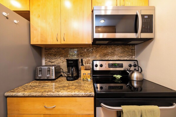 Une cuisine avec des meubles en bois, un four à micro-ondes en acier inoxydable, un grille-pain, une machine à café et une bouilloire posés sur une cuisinière noire.