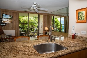 Enjoy meals in the kitchen with a large window offering a view of lush greenery and a dining area with wicker furniture.