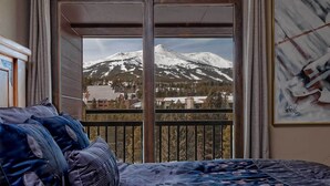 Une chambre avec une grande fenêtre donnant sur une montagne enneigée et sur une ville située en contrebas.