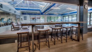 Un espace bar moderne avec de hauts plafonds, de grandes fenêtres et une vue sur les voitures garées à l’extérieur.