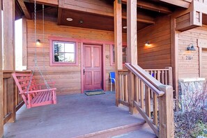 Une cabane en bois avec une véranda, une balançoire, une porte rouge et une chaise bleue.