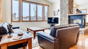 Un salon avec une cheminée en pierre, un canapé en cuir, une table basse en bois et un téléviseur.